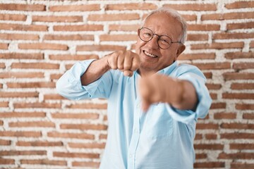 Sticker - Senior man with grey hair standing over bricks wall punching fist to fight, aggressive and angry attack, threat and violence