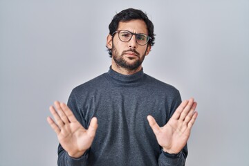 Canvas Print - Handsome latin man standing over isolated background moving away hands palms showing refusal and denial with afraid and disgusting expression. stop and forbidden.