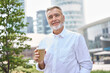 Confident mature older rich successful gray-haired business man leader, happy mid aged senior professional businessman holding coffee looking at camera standing outside in city park, portrait.