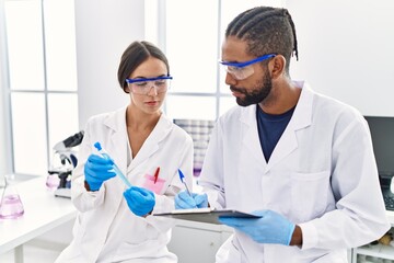 Sticker - Man and woman scientist partners holding test tube and writing on clipboard at laboratory