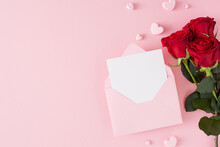 Women Day Concept. Flat Lay Photo Of Red Flowers, Envelope With Letter And Pink Heart Shaped Baubles On Pastel Pink Background With Copy Space. Mother Day Card Idea.