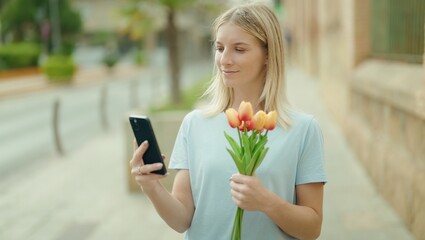 Sticker - Young blonde woman using smartphone holding bouquet of flowers at street