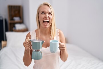 Sticker - Young caucasian woman drinking coffee on the bed angry and mad screaming frustrated and furious, shouting with anger looking up.