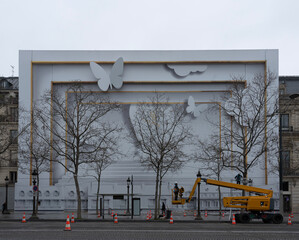 Paris, France - 01 12 2023: Avenue des Champs Elysees. View of the facade with decorated scaffolding and a yellow lift machine with a technician