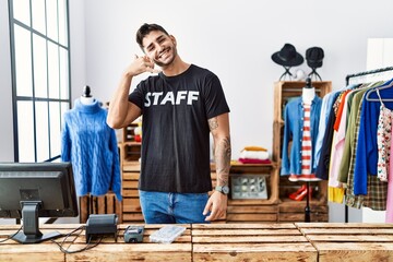 Canvas Print - Young hispanic man working at retail boutique smiling doing phone gesture with hand and fingers like talking on the telephone. communicating concepts.