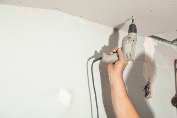 Poster - Worker with a drill screwdriver twists the screw into the drywall.