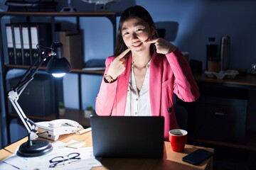 Wall Mural - Chinese young woman working at the office at night smiling cheerful showing and pointing with fingers teeth and mouth. dental health concept.