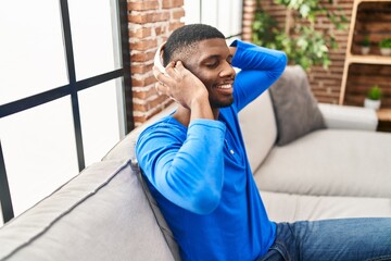 Wall Mural - Young african american man listening to music sitting on sofa at home