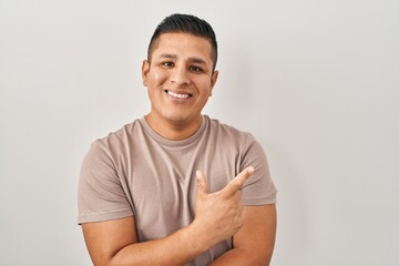 Canvas Print - Hispanic young man standing over white background with a big smile on face, pointing with hand and finger to the side looking at the camera.