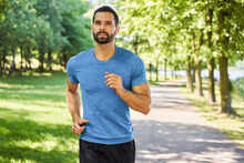 Active Young Man Running With Earphones In Park During Sunny Day In Spring Summer