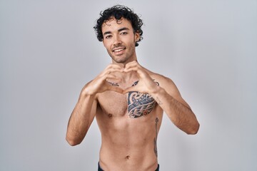 Sticker - Hispanic man standing shirtless smiling in love doing heart symbol shape with hands. romantic concept.