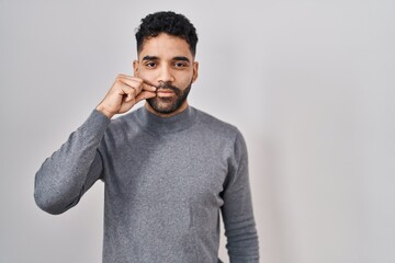 Poster - Hispanic man with beard standing over white background mouth and lips shut as zip with fingers. secret and silent, taboo talking