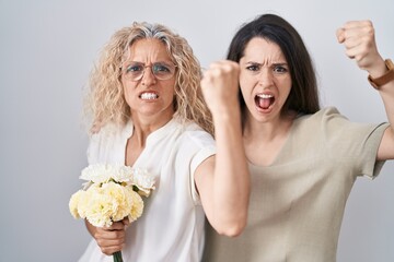 Sticker - Mother and daughter holding bouquet of white flowers angry and mad raising fist frustrated and furious while shouting with anger. rage and aggressive concept.