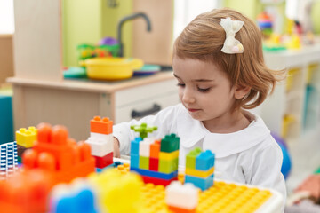 Sticker - Adorable caucasian girl playing with construction blocks sitting on table at kindergarten