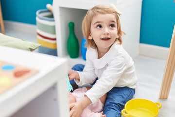 Poster - Adorable caucasian girl playing with baby doll sitting on floor at kindergarten