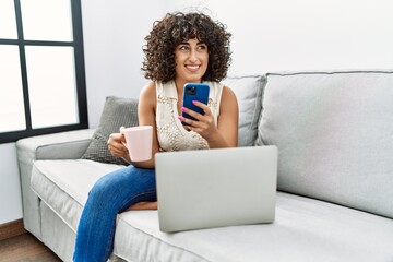 Sticker - Young middle east woman drinking coffee using laptop and smartphone at home