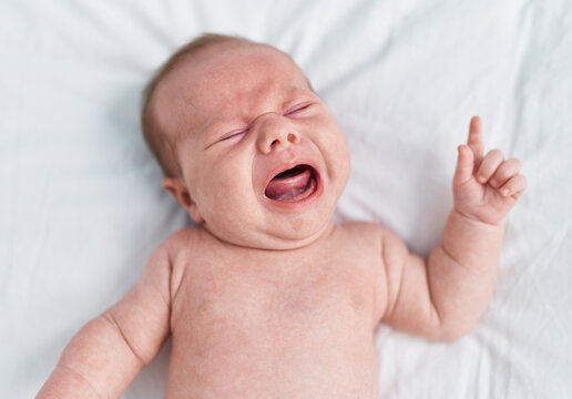 Adorable caucasian baby lying on bed crying at bedroom