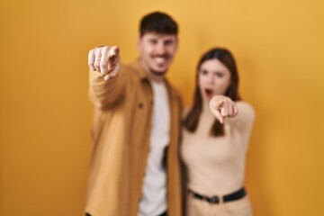 Sticker - Young hispanic couple standing over yellow background pointing displeased and frustrated to the camera, angry and furious with you