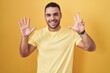 © Krakenimages.com - Young hispanic man standing over yellow background showing and pointing up with fingers number eight while smiling confident and happy.