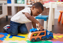 African American Boy Playing With Cars And Truck Toy Sitting On Floor At Kindergarten