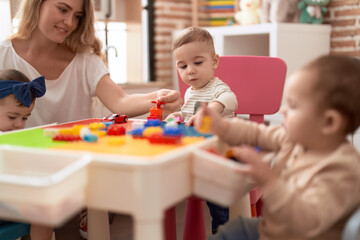 Poster - Teacher and preschool students playing with construction blocks sitting on table at kindergarten