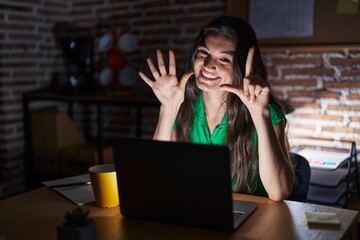 Sticker - Young teenager girl working at the office at night showing and pointing up with fingers number seven while smiling confident and happy.