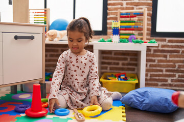 Poster - Adorable hispanic girl playing with hoops game sitting on floor at kindergarten