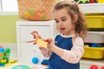 Poster - Adorable blonde girl student cutting paper sitting on floor at kindergarten