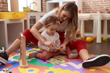 Poster - Teacher and toddler playing with maths puzzle game sitting on floor at kindergarten