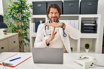 Wall Mural - Handsome middle age doctor man working at the clinic doing time out gesture with hands, frustrated and serious face