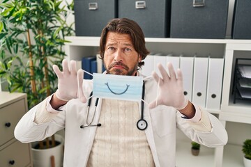 Wall Mural - Handsome middle age doctor man wearing safety mask depressed and worry for distress, crying angry and afraid. sad expression.