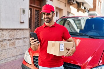 Sticker - Young hispanic man courier using smartphone holding package at street