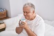 © Krakenimages.com - Middle age grey-haired man drinking cup of coffee sitting on bed at bedroom