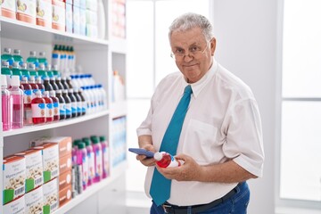 Wall Mural - Middle age grey-haired man customer using smartphone holding medicine bottle at pharmacy