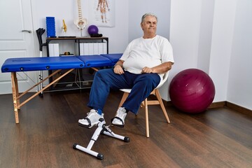 Canvas Print - Senior caucasian man at physiotherapy clinic using pedal exerciser looking away to side with smile on face, natural expression. laughing confident.