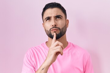 Wall Mural - Hispanic young man standing over pink background thinking concentrated about doubt with finger on chin and looking up wondering