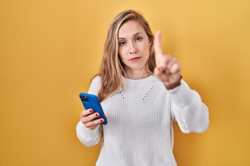 Poster - Young blonde woman using smartphone typing message pointing with finger up and angry expression, showing no gesture