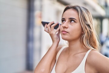 Poster - Young blonde woman listening audio message by the smartphone with serious expression at street