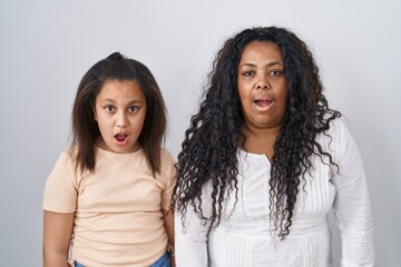 Sticker - Mother and young daughter standing over white background afraid and shocked with surprise and amazed expression, fear and excited face.