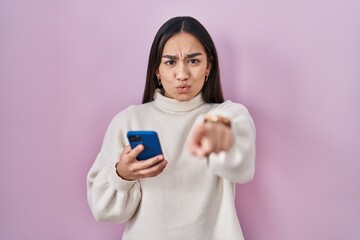 Canvas Print - Young south asian woman using smartphone pointing with finger to the camera and to you, confident gesture looking serious