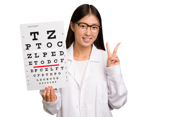 Wall Mural - Young asian oculist woman holding a eye chart paper isolated showing number two with fingers.