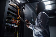 Backlit Side View Portrait Of Black Man Working With Server Cabinet In Data Center And Taking Notes On Clipboard, Copy Space