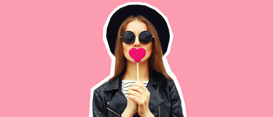 Portrait of stylish young woman with heart shaped lollipop posing wearing black round hat on pink background, magazine style