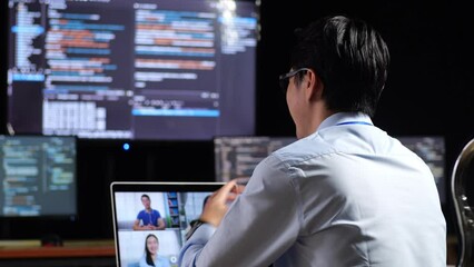 Close Up Back View Of Asian Male Programmer Having A Meeting By A Laptop While Writing Code On Multiple Monitors Showing Database On Terminal Window Desktops In The Office
