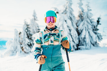 Woman in skiing clothes with helmet and ski googles on her head with ski sticks. Winter weather on the slopes. On top of a mountain and enjoying view. Alpine skier. Winter sport