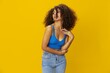 © SHOTPRIME STUDIO - Woman with curly afro hair in a blue t-shirt on. yellow background signs with her hands, look into the camera, smile with teeth and happiness, copy space