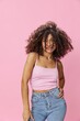 © SHOTPRIME STUDIO - Woman with curly afro hair dancing in pink top and jeans on pink background, smile, copy place