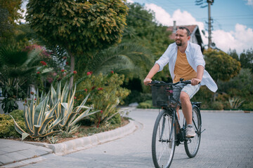 A young man rides a bicycle along a green street with private houses.  Eco-friendly transport.  Green mobility and transport