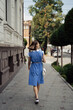 © diignat - Back view of a woman in a blue midi dress walking on the city street with an white purse. Lovely usual day