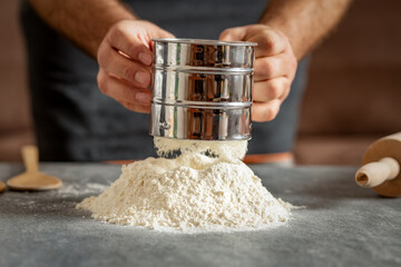 Poster - Man sifting flour for preparing bread dough in a bakery close up